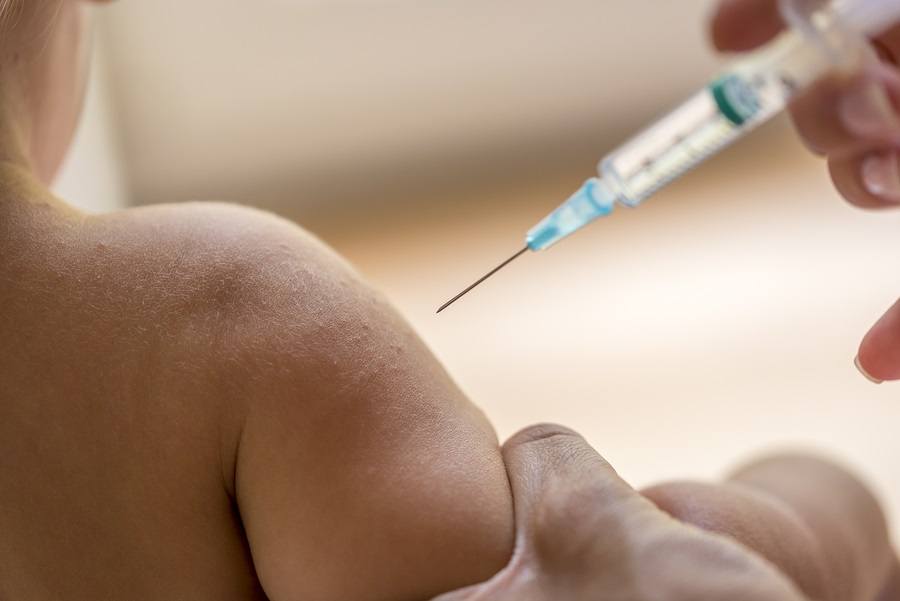 Doctor injecting a young child with a vaccination or antibiotic in a small disposable hypodermic syringe close up of the kids arm and needle.