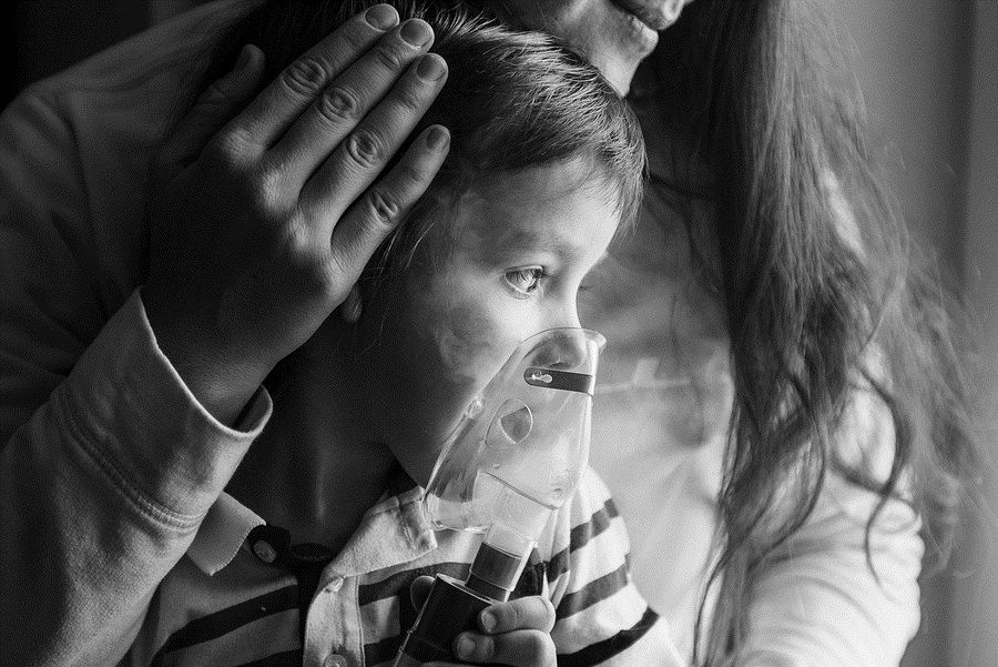 Photo of young woman with son doing inhalation with a nebulizer at home. Mother of a young child making inhalation