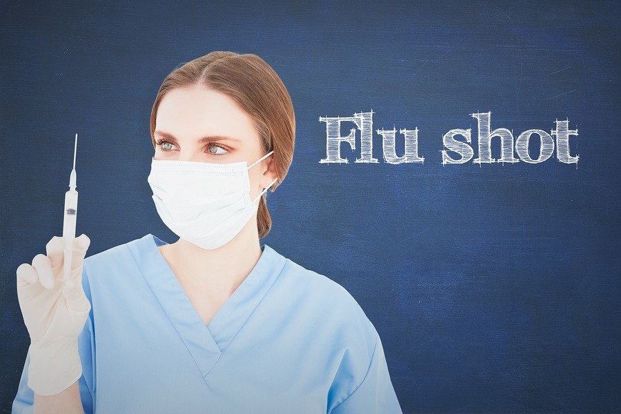 The word flu shot and female doctor holding a syringe and looking at it