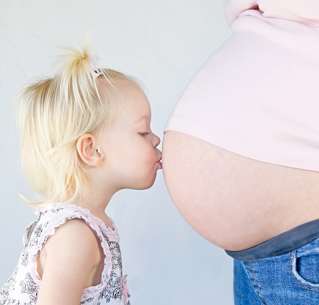 little girl kissing belly of pregnant mom photo