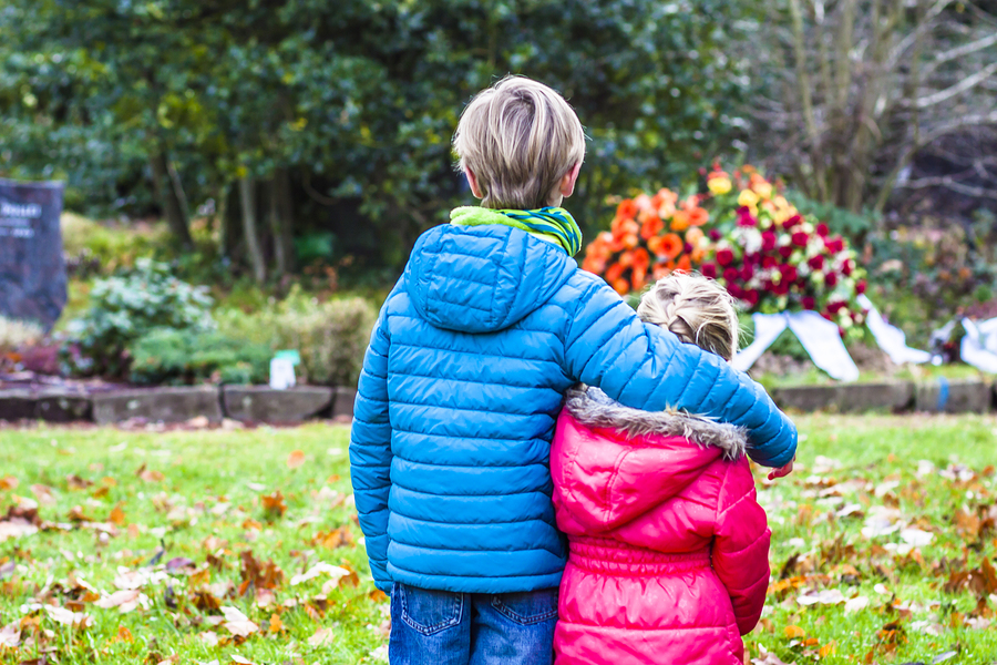 Little brother and sister standing at the grave of their parents in the graveyard