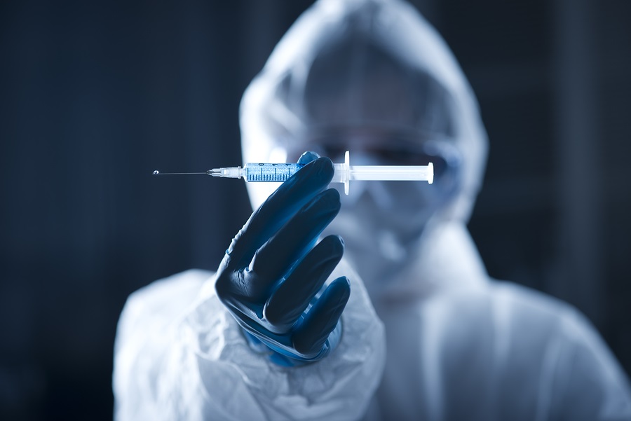 Researcher in hazmat protective suit preparing a syringe for injection.