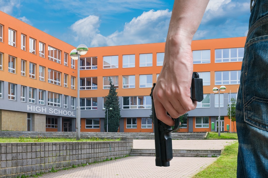 Young armed man holds pistol in hand in public place near high school.