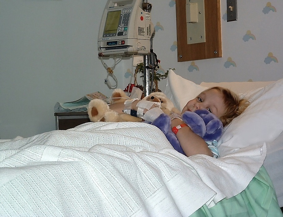 a little girl in a hospital bed with stuffed animals