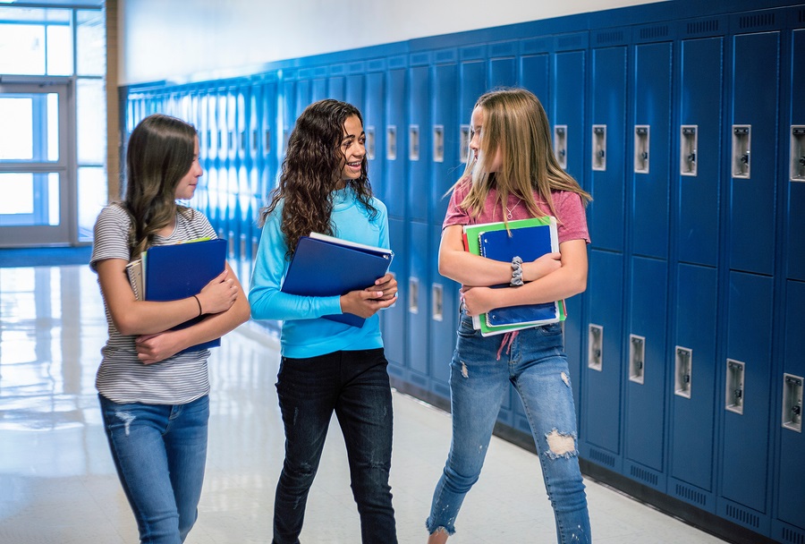 Candid photo of Three Junior High school Students talking together in a school hallway. 